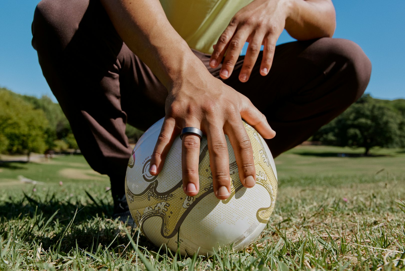 Hand on top of a soccer ball wearing an Oura Ring