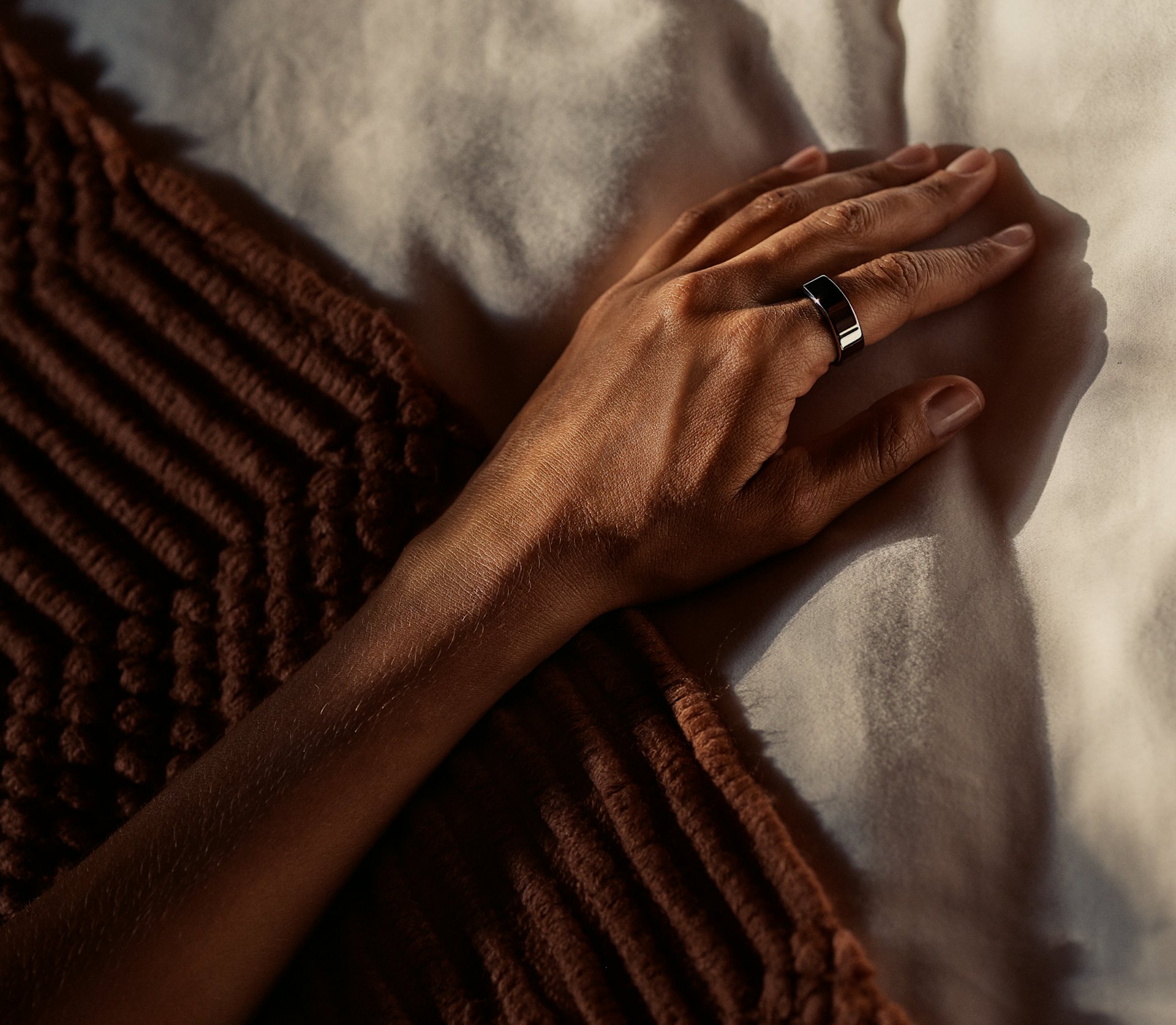 A hand on a bed wearing an Oura ring.
