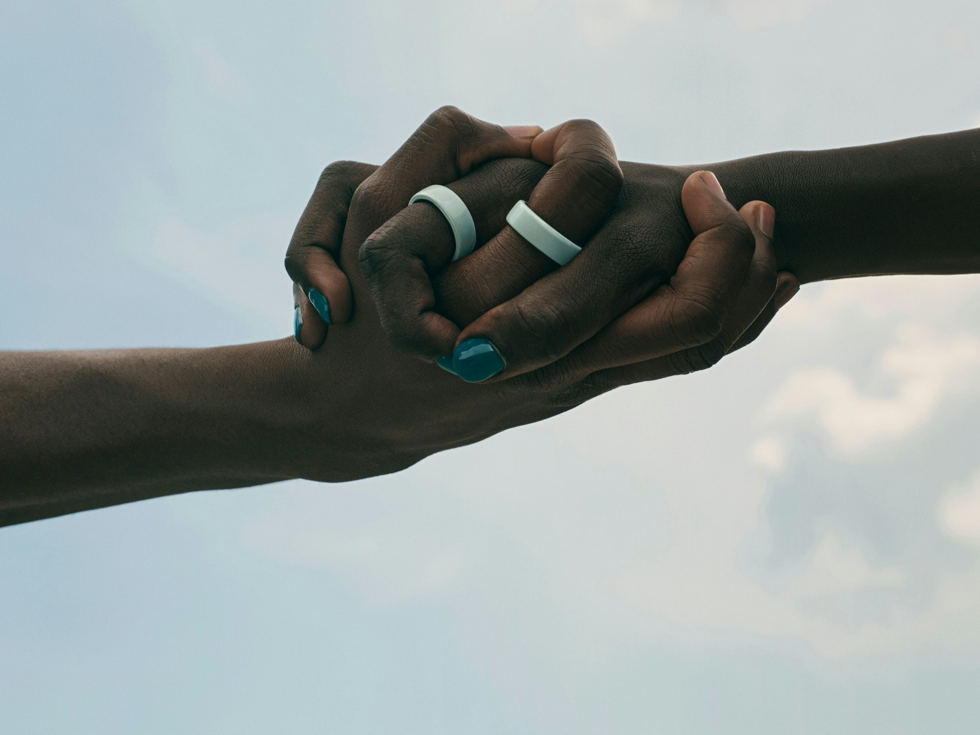 A close-up of two hands holding each other, each wearing an Oura Ring 4 Ceramic on the index finger.